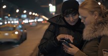 Women watching something on mobile while waiting at bus stop