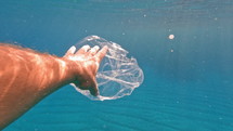 Person grabbing plastic from underwater.