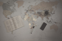 Bible, marker, cellphone, and coffee mug on a world map 