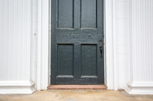 Black rustic painted door entrance to church surrounded by white siding