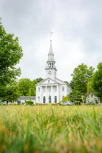 View from the grass of the front exterior of white New England church building on Cheshire green in Connecticut with steeple and pillars