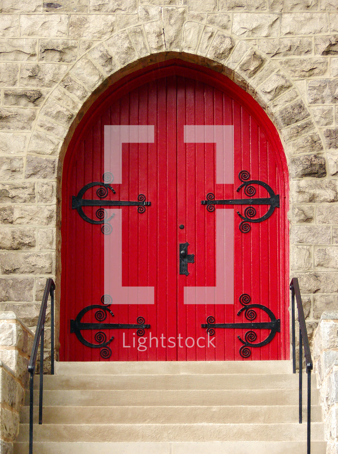 stone wall frames arched red door with decorative metalwork