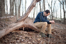 Man sitting outside and praying with folded hands and bowed head in the forest on a fallen tree log