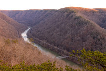 View of winding river in canyon flowing through dense tree covered mountains at New River Gorge National Park during sunset