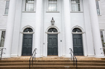 Front of Cheshire town church building with staircase and three black doors with transoms and tall white column pillars 