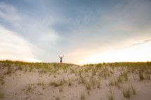 Man worshiping with raised outstretched arms looking out at sky on top of sandy grassy hill 