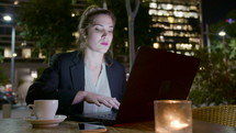 Young business woman sitting in a cafe at night, working on a laptop computer