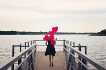 a woman walking carrying helium balloons on a dock 