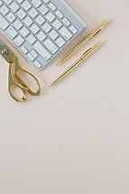 gold scissors, gold pens, and computer keyboard on a pink background 