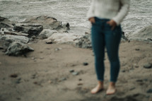 a woman in jeans standing on a beach 