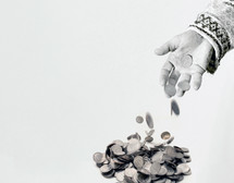 A person's hand throwing coins into a pile
