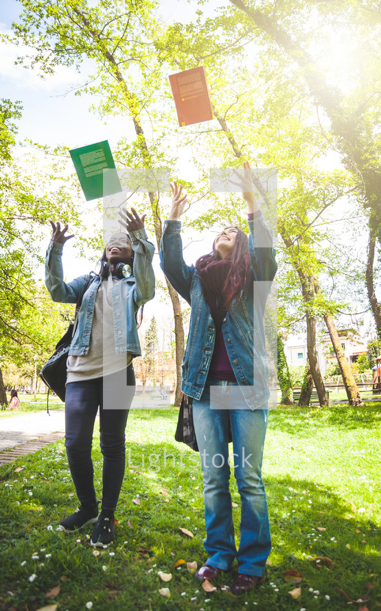 Two female students, one Caucasian and the other African American, throw books into the air. End of studies concept.