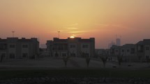 Sun setting behind buildings and homes in city of Dubai in suburban housing area.
