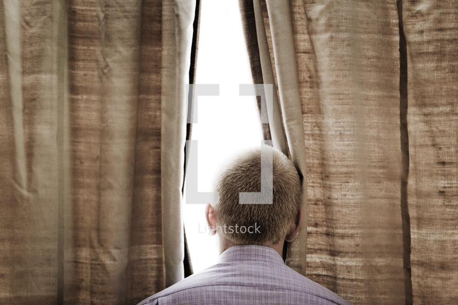 man looking through curtains of a window