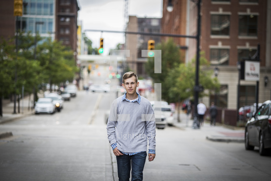 teen boy walking down the center of a city street 