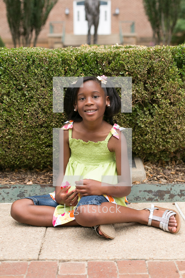 Smiling girl sitting down on sidewalk.