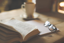 a notebook, reading glasses, coffee cup, and an open Bible on a desk 