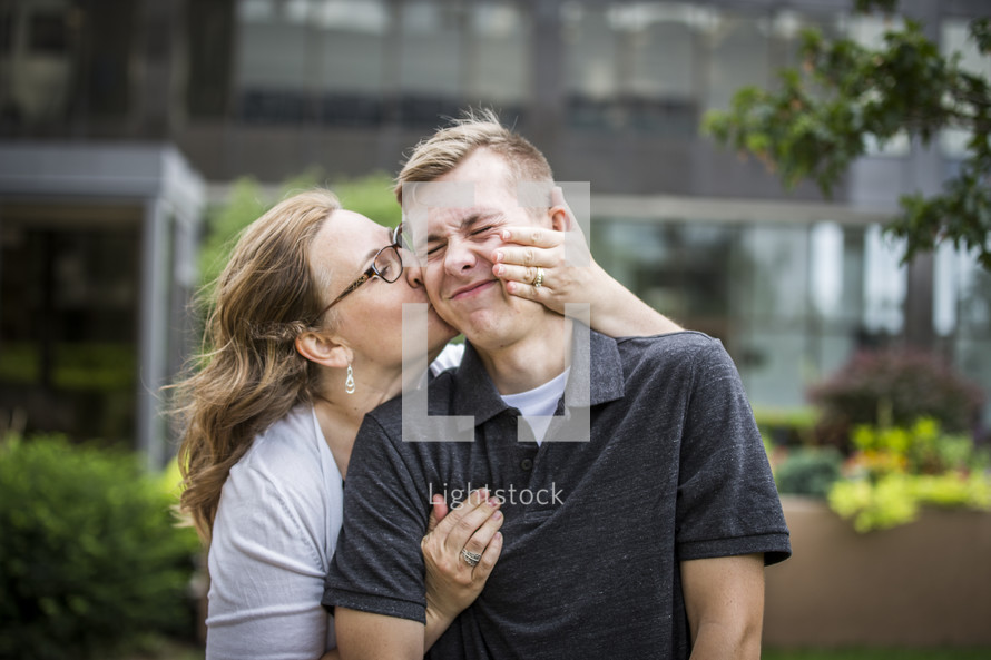 mom kissing her teenage son on the cheek 