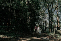 a bride and groom walking down a dirt path 