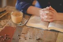 a woman reading at a table and praying hands over the pages of a Bible 