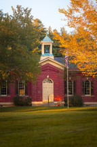 Front exterior of old traditional red brick schoolhouse during autumn 