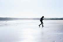 a boy child running on a beach in a coat 