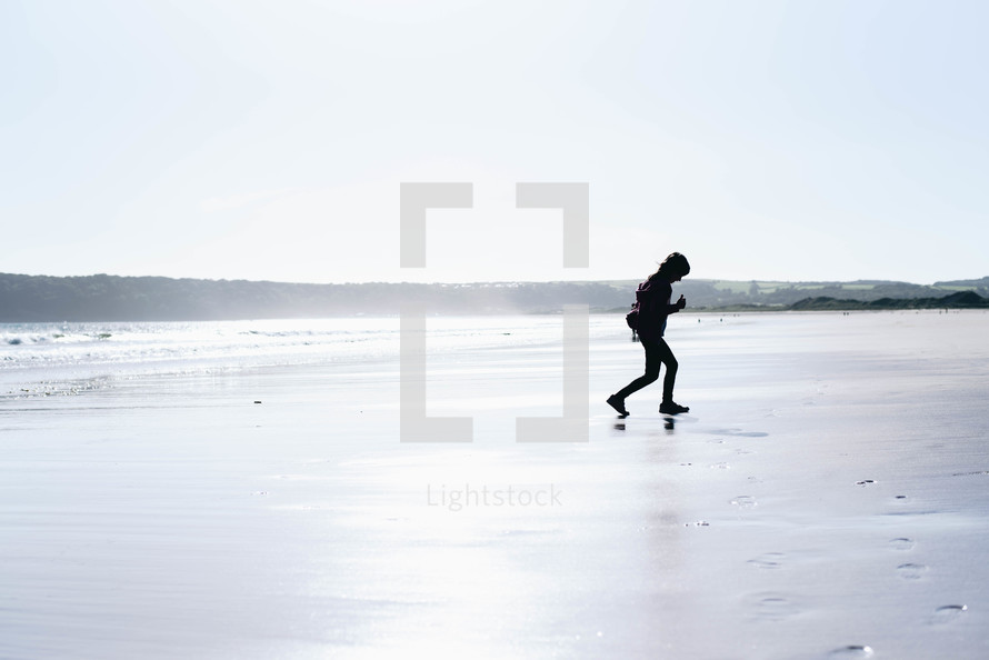 a boy child running on a beach in a coat 