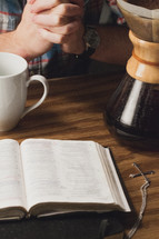 Praying over coffee and a Bible on a wooden table.