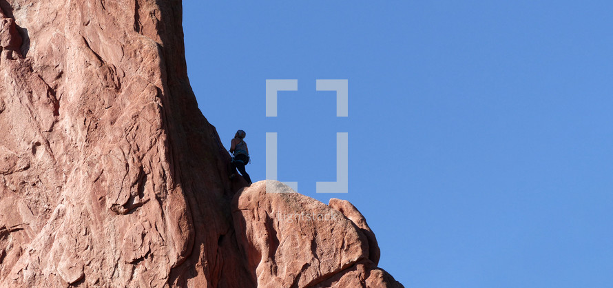 rock climber on large rock with blue sky background