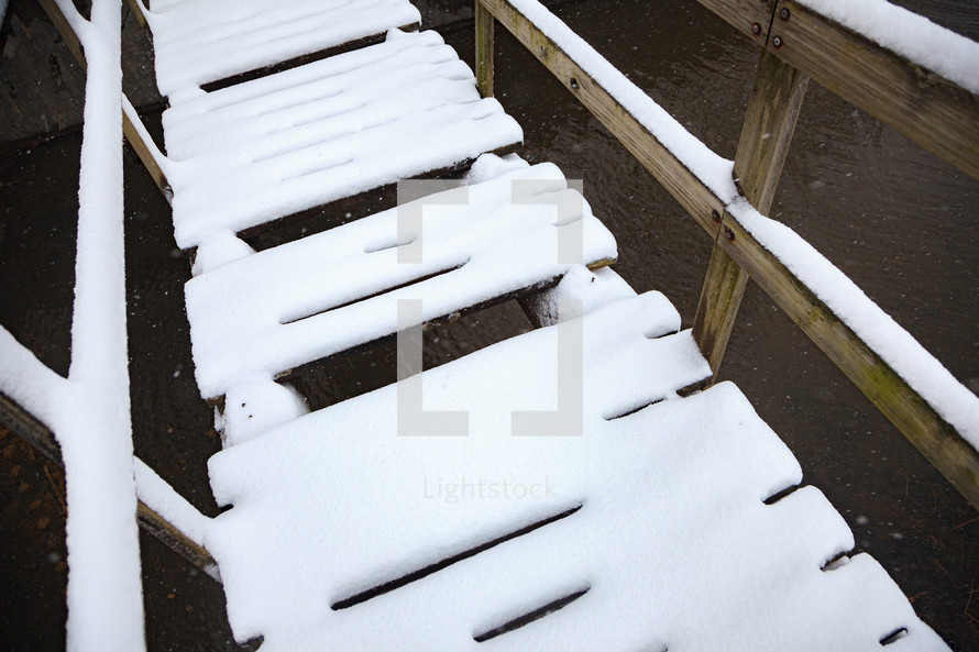 Wooden footbridge covered with snow over water 