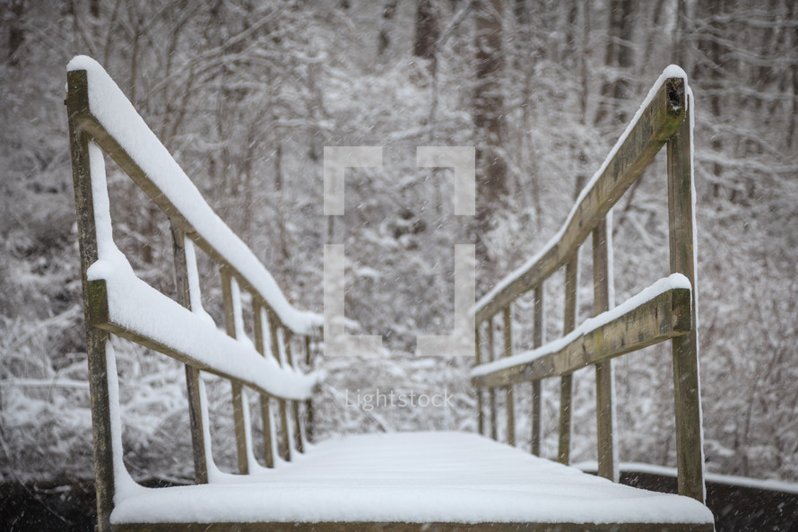 low angle of a wooden footbridge covered with snow with trees in the background