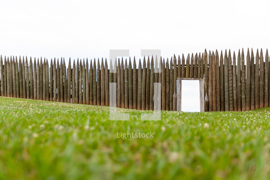 Entrance opening in wooden picket fort fence on green grassy lawn