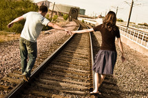 man and a woman walking on railroad tracks holding hands