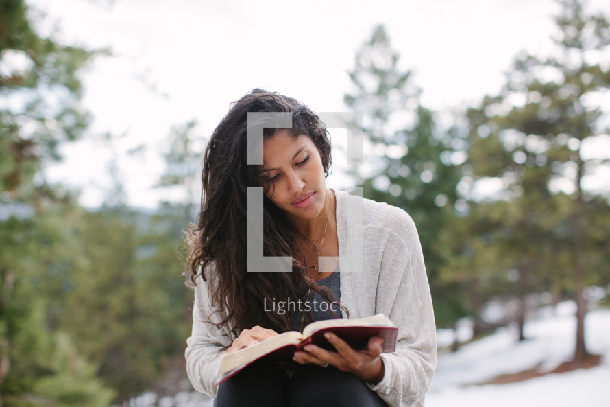 a young woman reading a Bible on a snowy mountaintop 