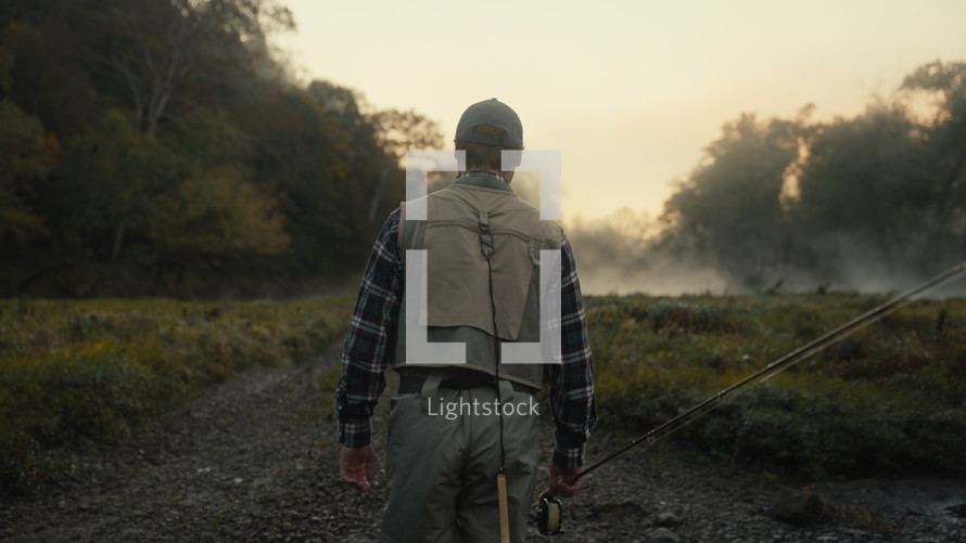 Young fly fisherman walking to a river at dawn