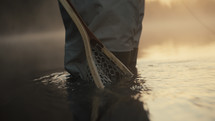 Fly fisherman’s net resting in a river during sunrise