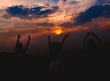 girls with raised hands standing outdoors at sunset 