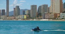 Two people on a jet ski in a beach with high-rise buildings in the background—Benidorm, Spain.