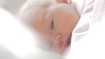 Close-up shot of a quiet newborn baby girl wrapped in a light blanket.