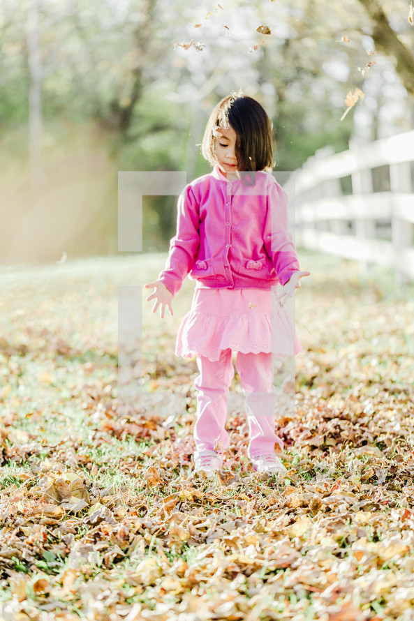 a young girl playing in fall leaves 