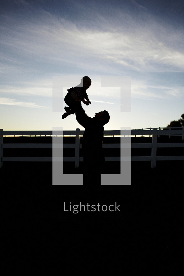 silhouette of a father holding up his son 