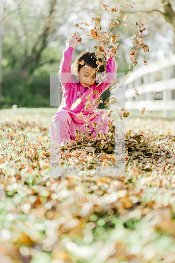 a young girl throwing through fall leaves 