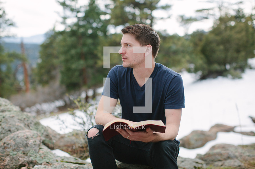 a man sitting on a rock reading a Bible