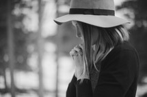 a woman in prayer wearing a hat 