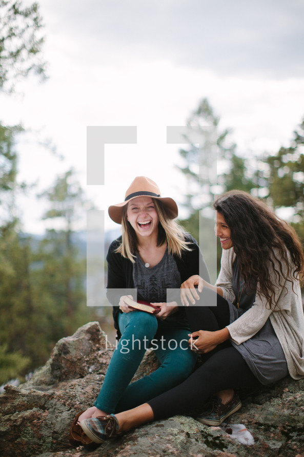 friends sitting on a rock reading a Bible with joy