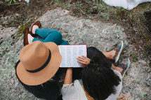 a couple sitting on a rock reading a Bible 