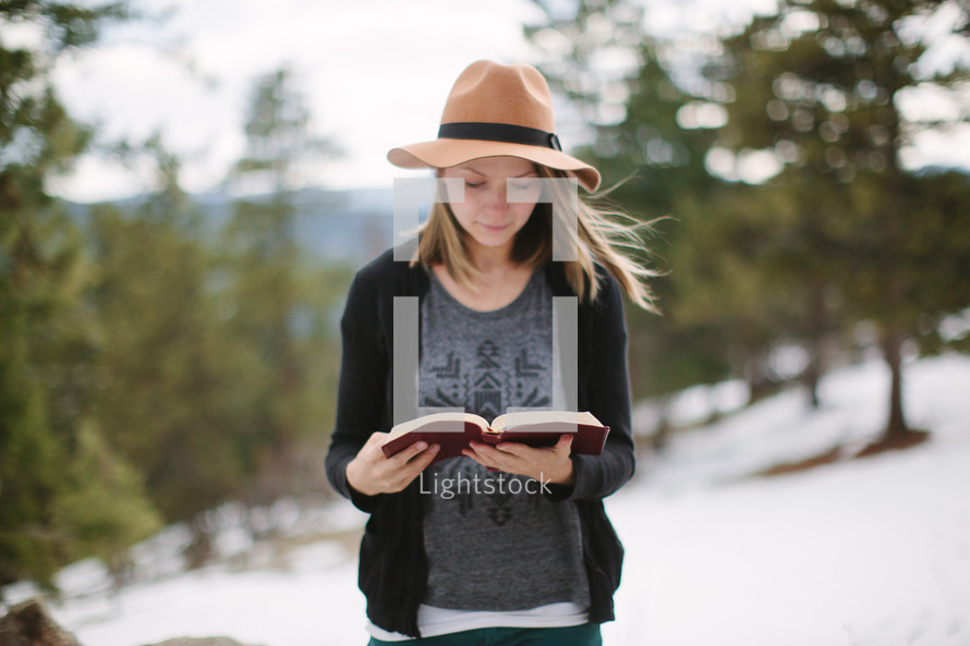 a young woman reading a Bible outdoors in snow 