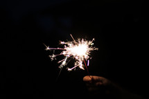 A hand holding a lit sparkler in the darkness.