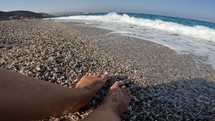 Ocean waves crashing on woman's feet on rocky beach