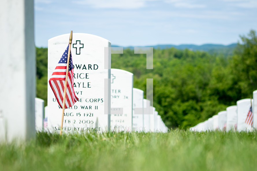 American flag stuck in ground in front of white military gravestone memorials in rural cemetery